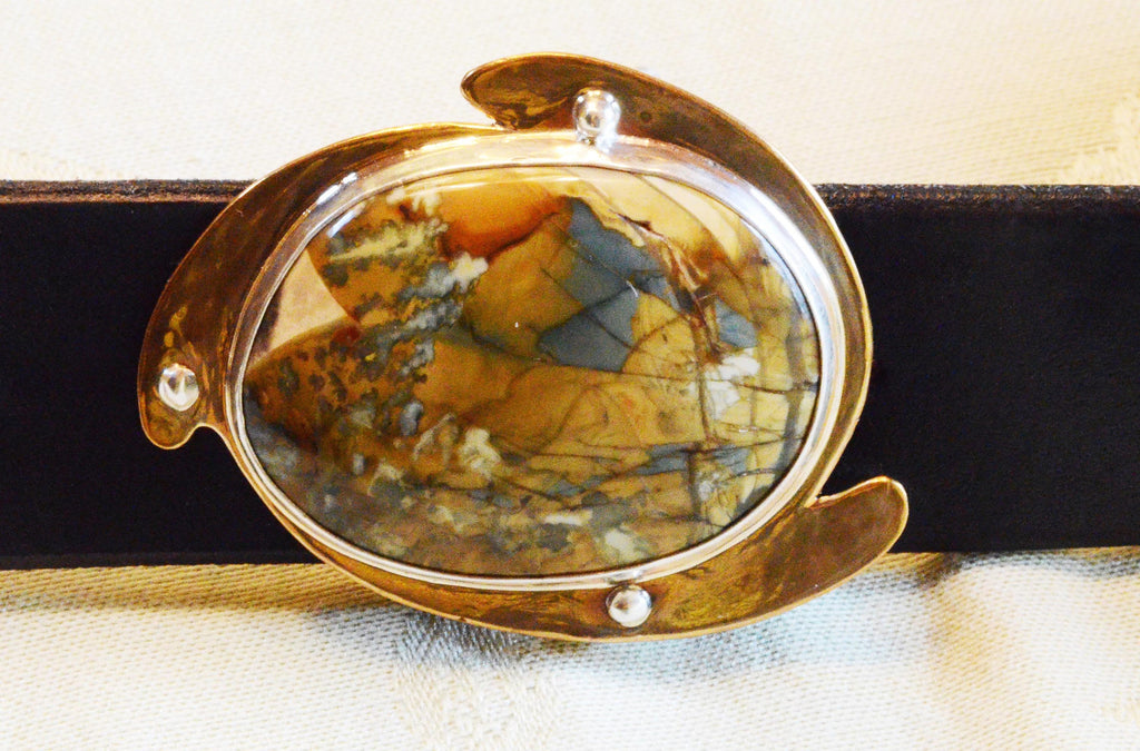 Close-up of morrisonite jasper belt buckle. The stone is oval-shaped and colorful, with a mix of gray-blues, orange, gold and white figuring.